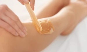 Beautician waxing female legs in spa center