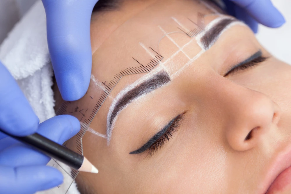Permanent make-up for eyebrows of beautiful woman with thick brows in beauty salon.